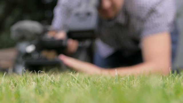 The cameraman lying on the green grass is videotaping