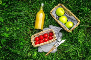 Summertime picnic concept. Light meal. Appetizers. Apple, bottle of juice, tomatoes on green grass top view copy space
