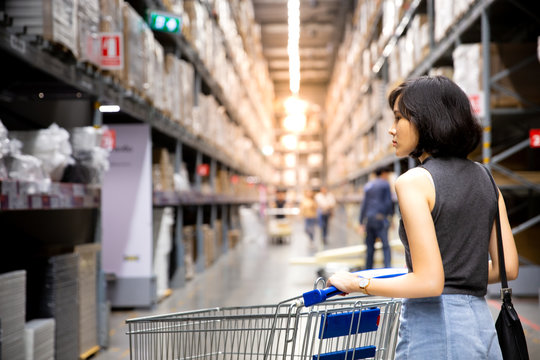 An Asian Woman Doing Shopping  And Walking With Her Cart In Cargo Or Warehouse.