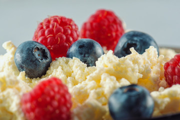 Cottage cheese with fresh raspberries and blueberries for a healthy breakfast with ripe berries. Background is a natural healthy product.