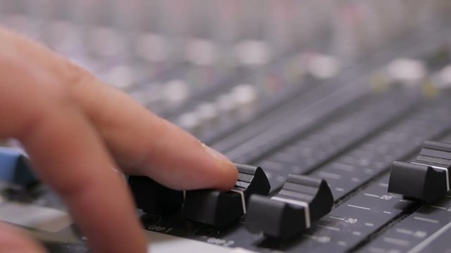 Hands of Audio engineer working on a professional analog console, moving faders, mixing music