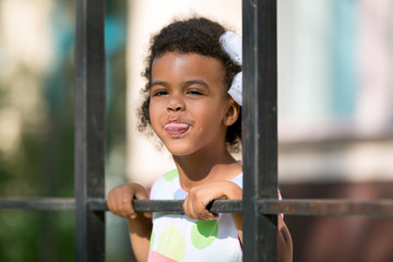 A black girl pokes her head through the fence.  A little African American girl holds onto the railing of the fence.