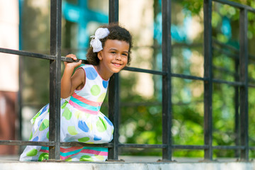 A black girl pokes her head through the fence.  A little African American girl holds onto the railing of the fence.