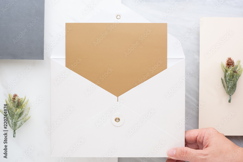 Aufkleber Top view of hand holding blank gold card in white envelop with pine leaf on two layer step of marble table top.Mock up template for display of design .luxury business items.