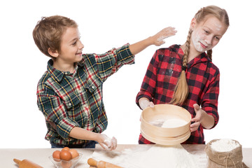 two children cheerfully cook pastries, indulge, sprinkle each other with flour, on a white...