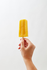 A woman's hand holds a yellow yoghurt ice cream lolly on a white background with copy space. Healthy food. Business concept concept