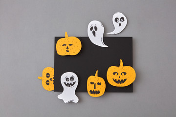 Black frame of flying ghosts, spirits and yellow scary pumpkins, handcraft from paper on a gray background. Flat lay