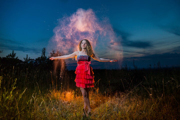 A girl in a black top and red skirt conjures up in a field during photoshoot with flour during sunset