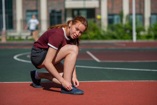 A young woman stopped to tie a string while running in the stadium. a red-haired student untied the lace during the lesson of physical education.