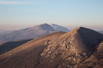 A view of some mountains top, beneath an empty blue sky at golden hour