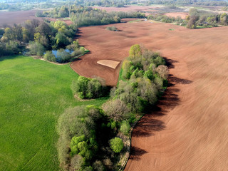 spring farmland  with fields, groves and pond, aerial view