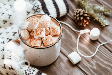 Hot cocoa with marshmallow in a white ceramic mug surrounded by winter things on a wooden table. The concept of cosy holidays and New Year.