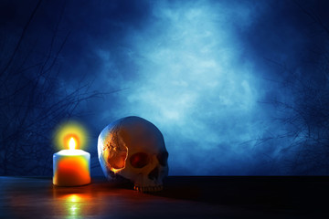medieval and fantasy halloween concept. Human skull and burning candle over old wooden table at...