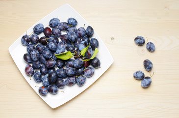 Fresh plums with leaves on a wooden table background. Flat lay composition.