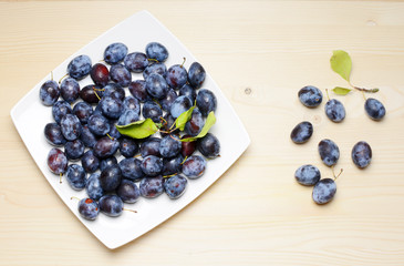 Fresh plums with leaves on a wooden table background. Flat lay composition.