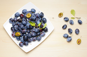 Fresh plums with leaves on a wooden table background. Flat lay composition.