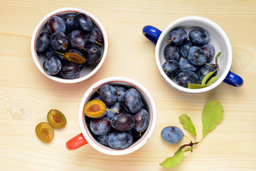 Fresh plums with leaves on a wooden table background. Flat lay composition.