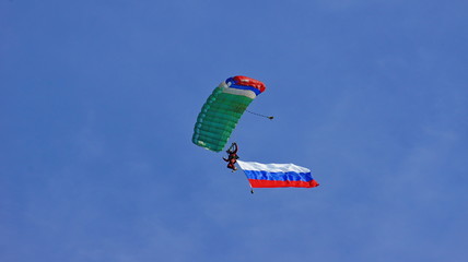 skydiver flying on the blue sky background with a large Russian flag which flutters in the wind