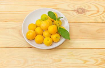 Yellow cherry plums on white saucer on wooden surface