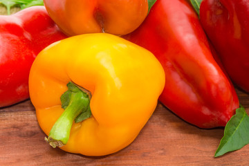 Yellow bell pepper against of red peppers on wooden surface