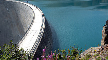A Panoramic view of a lake and Dam in the high alpine peaks of Switzerland. The lake is clear blue...