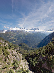 Fototapeta premium Stunning snow capped peaks of the Alpine ridge of the Mont Blanc Massive. The village of chamonix is visible on the valley floor. The mountain sides are lush green with pine forests on a summer day.