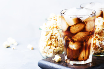 Sweet soda with ice cubes and caramel popcorn, gray background, selective focus