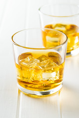 Glass of alcoholic drink with ice cubes on white table.