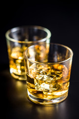 Glass of alcoholic drink with ice cubes on black table.