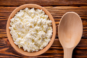 homemade cottage cheese in a wooden bowl, a wooden spoon lay on a wooden table