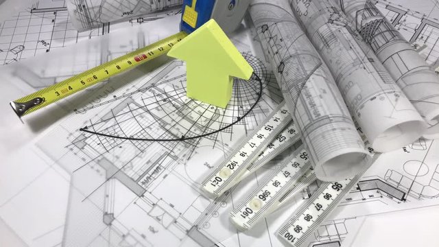 Blueprints - rolls of architectural drawings, roulette, yardstick - folding ruler and house symbol from a pack of yellow stickers smoothly rotate on the surface of the architectural drawings