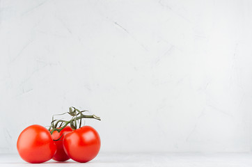 Group ripe red glossy tomatoes on green branch on white wooden background, copy space.