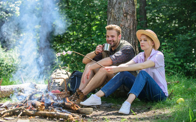 Roasting marshmallows at bonfire. Couple in love camping forest roasting marshmallows. Couple friends prepare roasted marshmallows snack nature background. Hike picnic. Couple eat snacks and drink