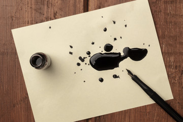 An overhead photo of an ink well with drops of ink and a nib pen, with copy space, on a dark rustic...