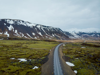 aerial view of road between fields and mountains with snow, snaefellsnes, iceland