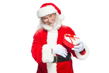 Christmas. Smiling Santa Claus in white gloves holds a red and white heart-shaped gift box with a red ribbon. Isolated on white background.