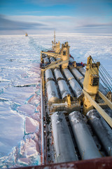 A cargo ship in the northern sea moves along the path laid by an icebreaker..