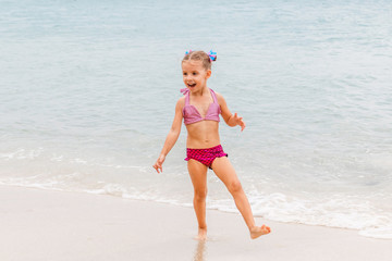 Fototapeta na wymiar Little beautiful girl dressed in swimsuit stands on the seashore