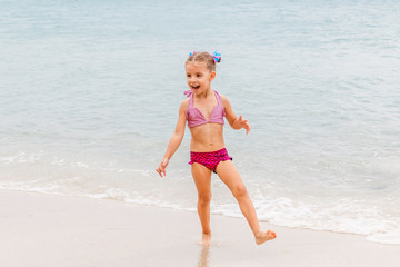 Little beautiful girl dressed in swimsuit stands on the seashore