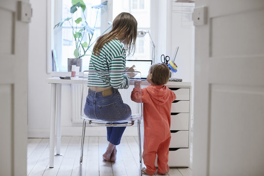 Rear view of girl standing by mother using laptop at table