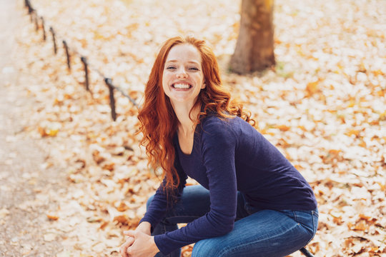 Cute young redhead woman sitting in an autumn park