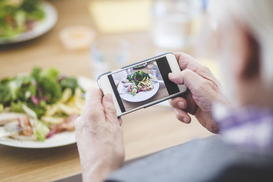 Cropped image of senior man photographing food through mobile phone at table