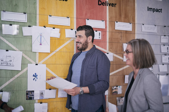 Smiling male and female business professionals holding documents while standing by notes on wall