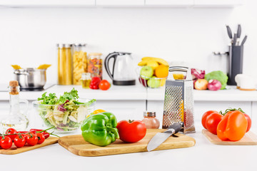 ripe vegetables, knife and grater on table in light kitchen