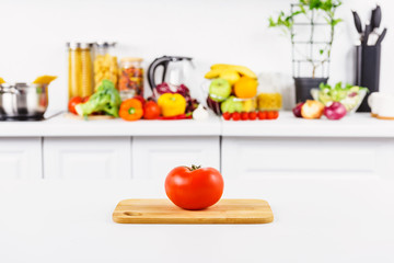 ripe tomato on cutting board with vegetables on background in light kitchen