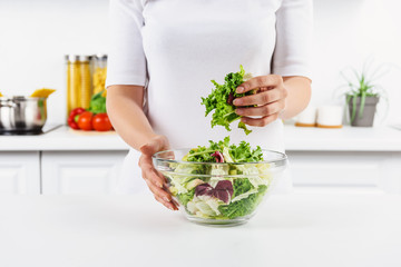 cropped image of woman holding bowl with salad leaves in light kitchen