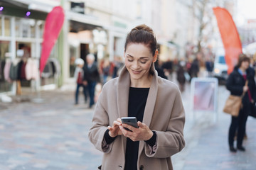 Young smiling woman wearing grey coat using phone