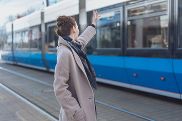 Stylish woman waving at a passing tram