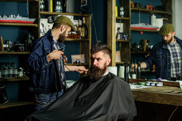 Barber preparing hair clipper for bearded man, barbershop background. Barber with clipper and...