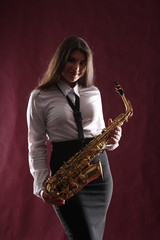 Obraz na płótnie Canvas Young girl with saxophone in studio on dark background